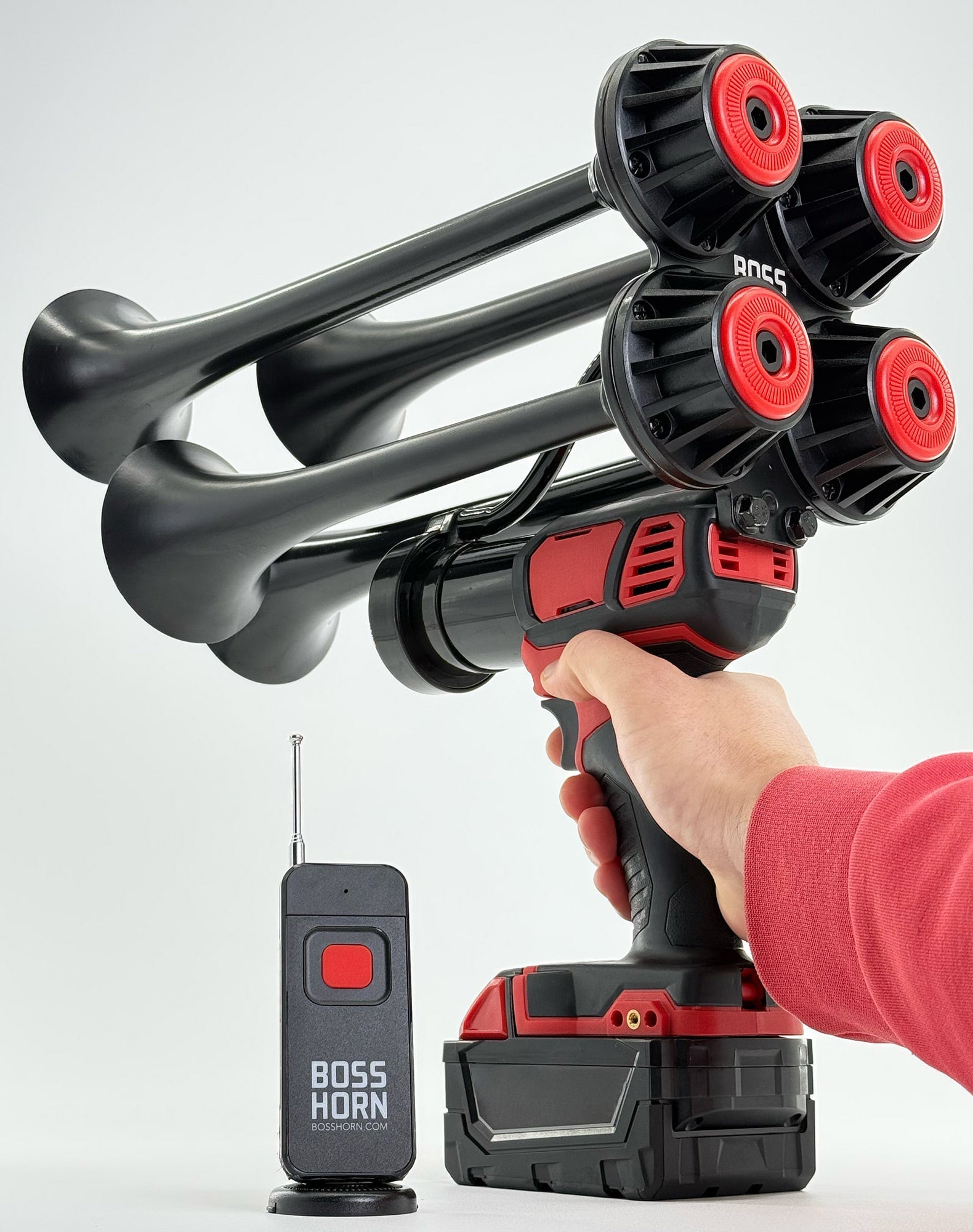 Hand holding the black quad-trumpet horn with red caps on a Milwaukee® M18 battery, antenna remote beside it on a light backdrop - view 13