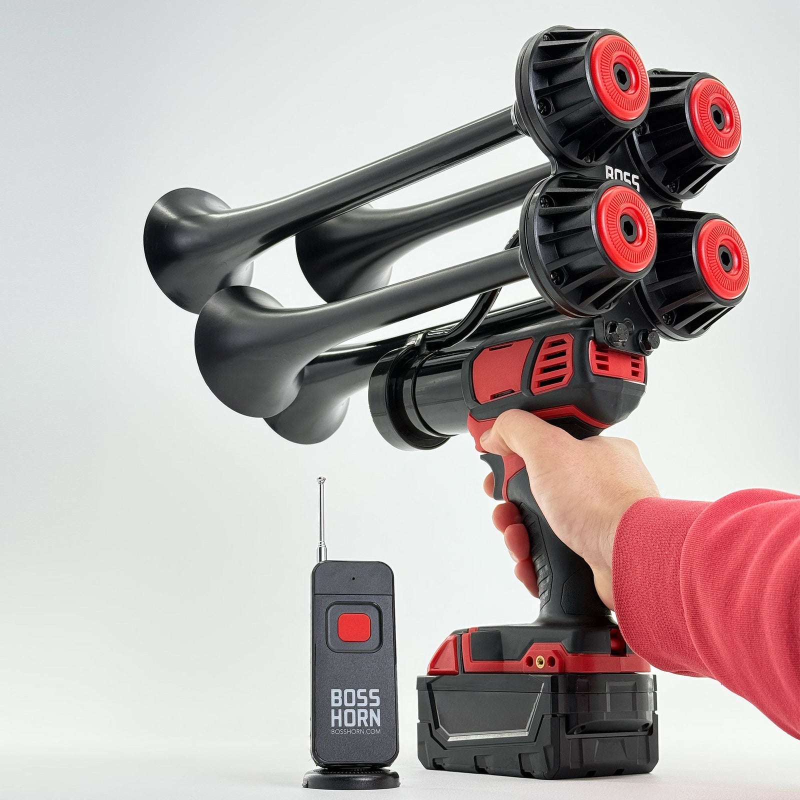 Hand holding the four-trumpet horn powered by a Milwaukee® M18 battery, wireless antenna remote beside it on a light background - view 10